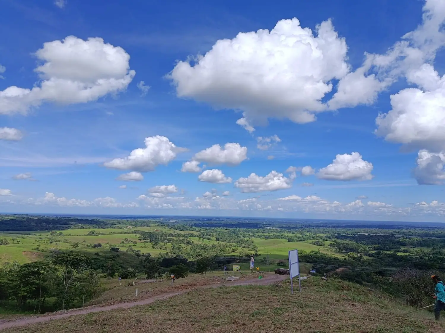 Panorámica del llano desde un lote de Le Mont Reserve: pastos verdes, cielo abierto con nubes y una trocha al fondo